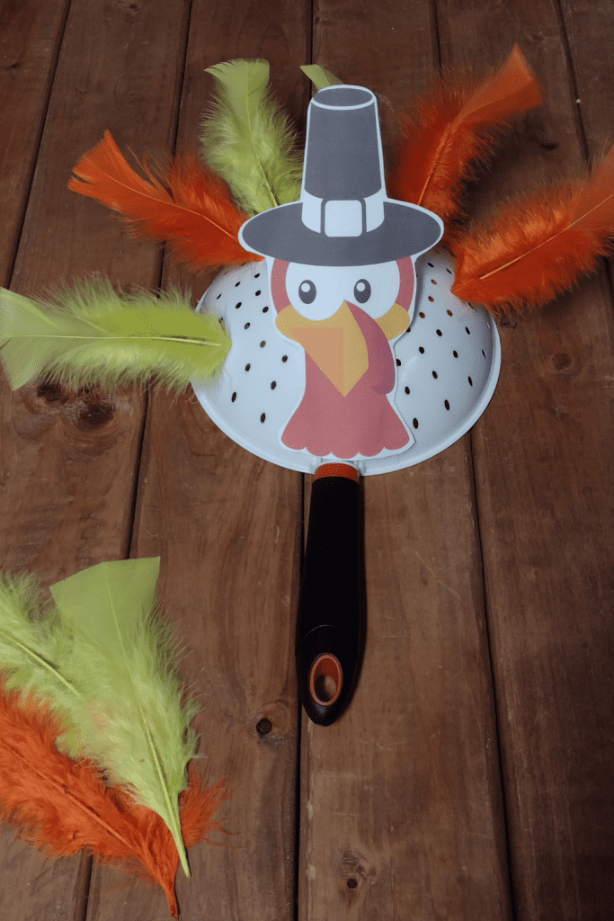A strainer with a turkey head taped to it and feathers in the strainer holes.