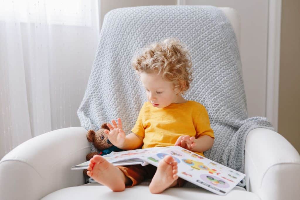 A boy sitting in a chair reaidn a book.