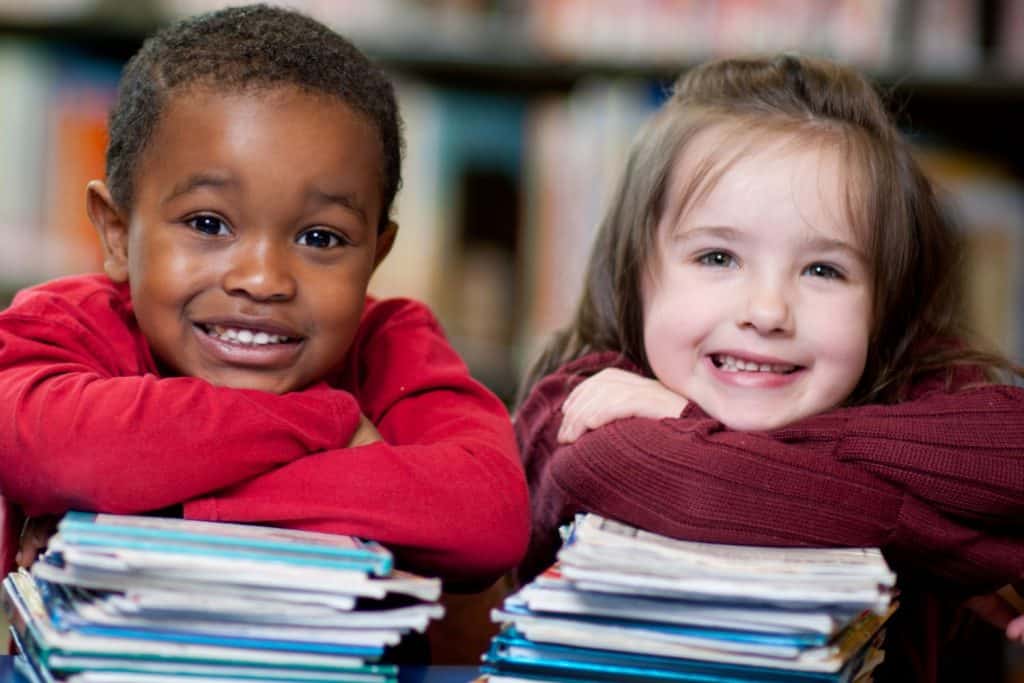A preschool boy and girl each resting their arms on a stack of book