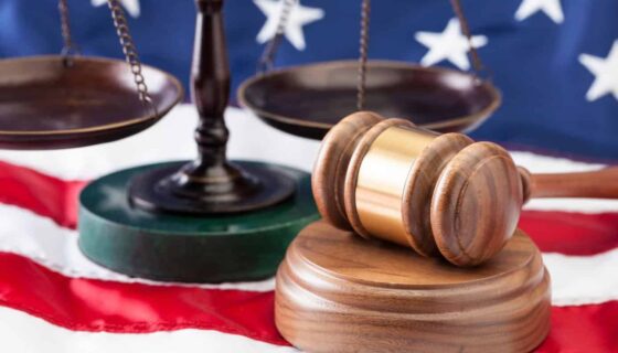 US flag background, metal balance scale and wodden gavel