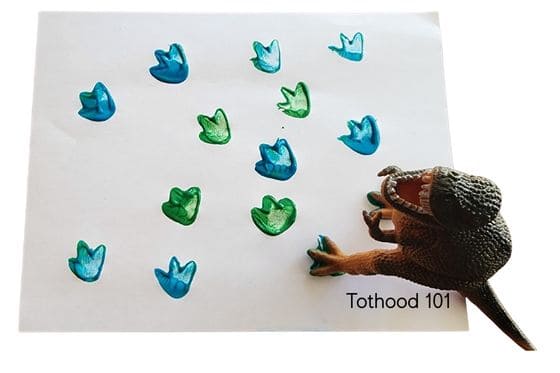 Plastic dinosaur with feet dipped in paint and painted footprints on paper